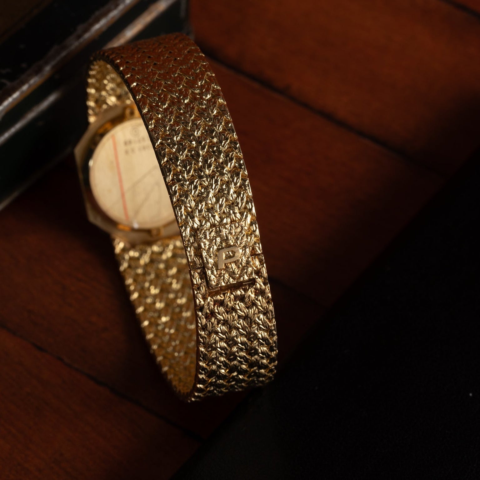 A Piaget Onyx Dial gold wristwatch with a textured band and P logo rests on a wooden surface.