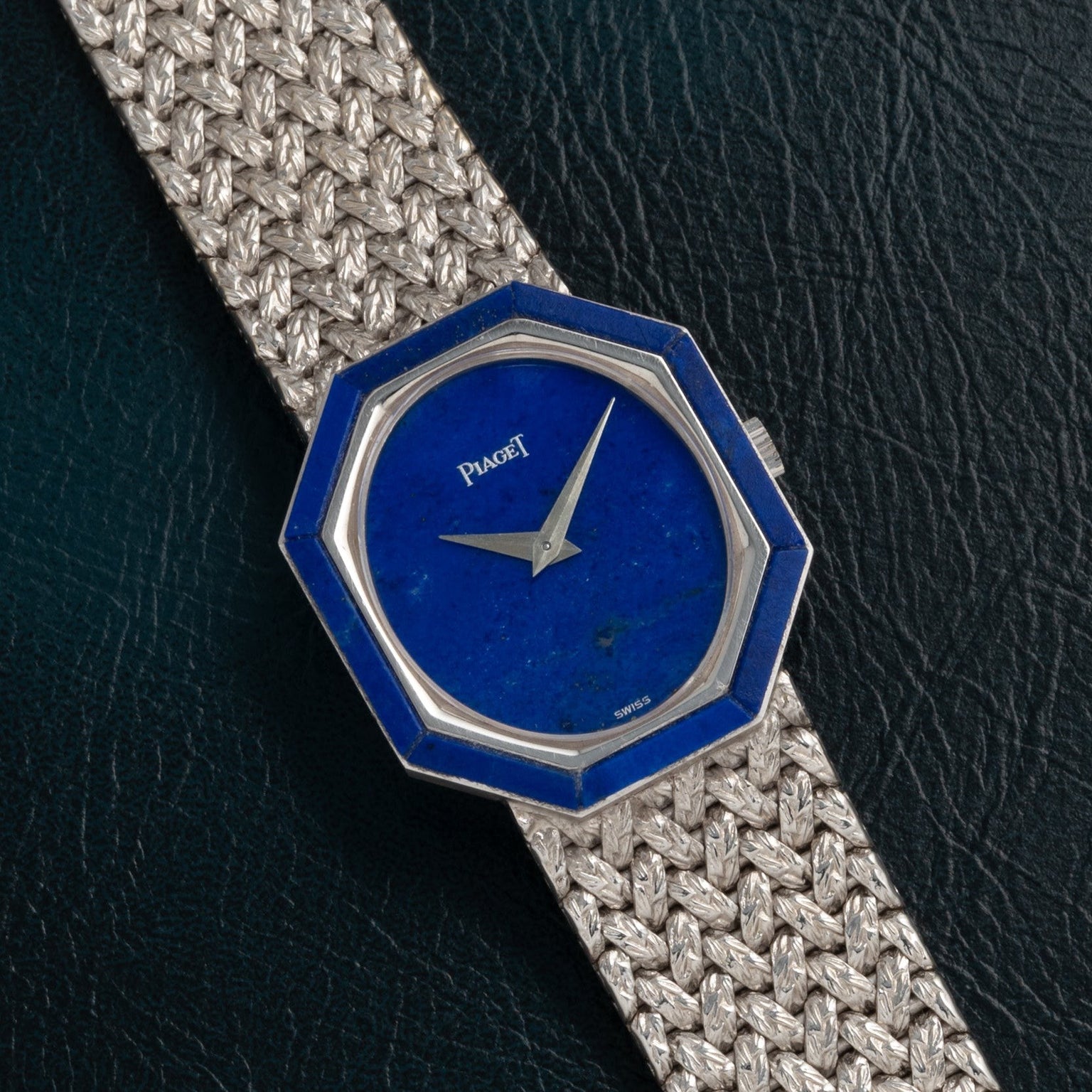 Piaget Lapis Lazuli White Gold Dress Watch with a hexagonal blue face and woven metal band displayed on a dark textured surface.