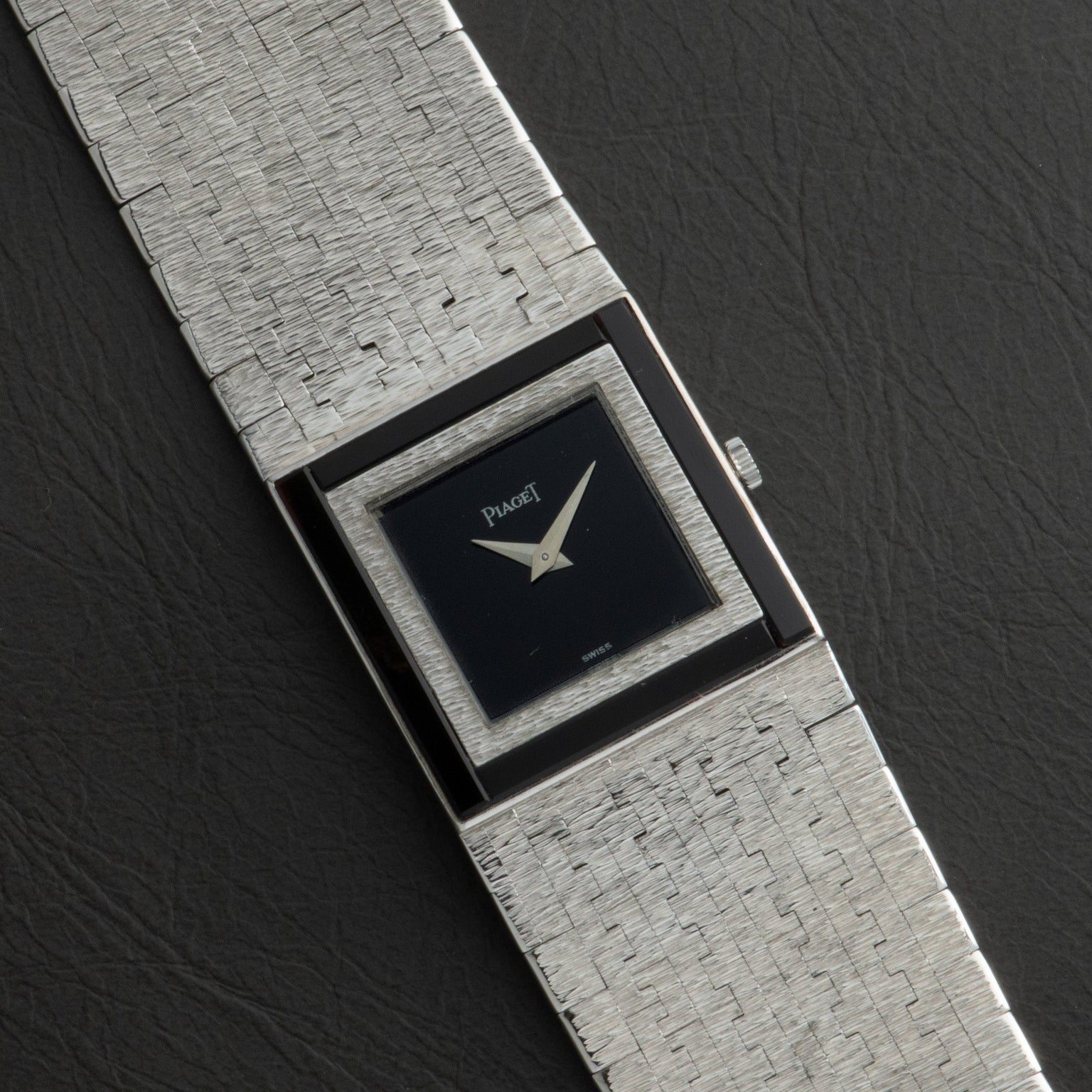 A Piaget White Gold Onyx Dress Watch with a textured band and black square dial is displayed on a dark surface.