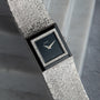 A Piaget White Gold Onyx Dress Watch with a textured band and rectangular black dial is displayed on a gray marble surface.