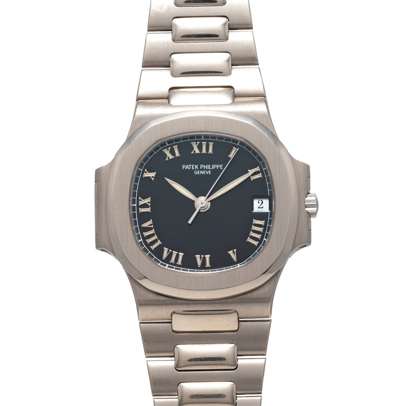 The Patek Philippe Nautilus is a silver wristwatch featuring a black face, Roman numerals, and a date window at 3 oclock.