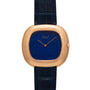 The Piaget Black Tie Andy Warhol watch features a blue lapis lazuli dial, gold case, and black leather strap, shown from the front.
