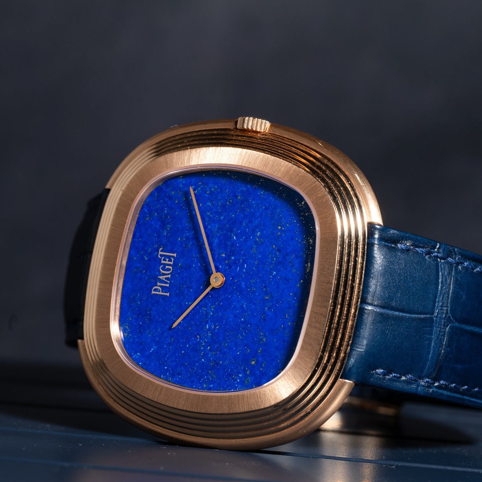 The Piaget Black Tie Andy Warhol watch features a blue lapis dial and blue leather strap, elegantly displayed on a dark surface.