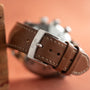 Close-up of a brown leather Jaeger-LeCoultre Tribute to Polaris watch strap, featuring the brands name engraved on the silver buckle, set against a peach background.