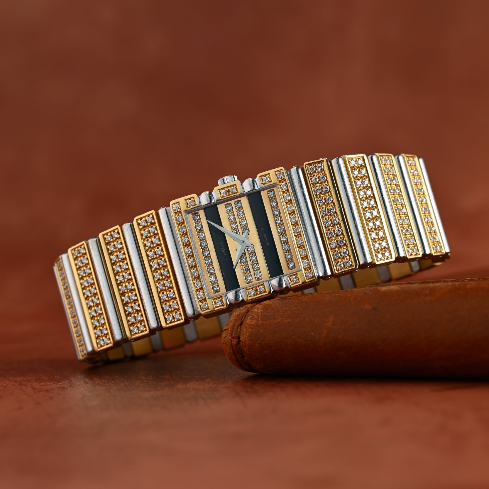 The Piaget Polo Pave, a luxurious gold and silver diamond-encrusted wristwatch, rests on a brown leather surface.