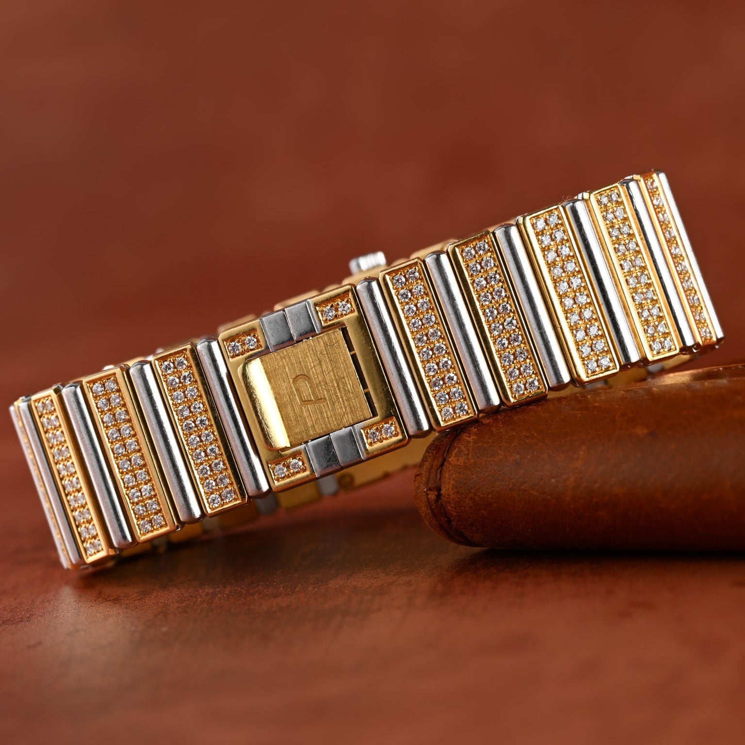 The Piaget Polo Pave bracelet features rows of sparkling diamonds set in gold and silver, elegantly displayed on a brown leather surface.