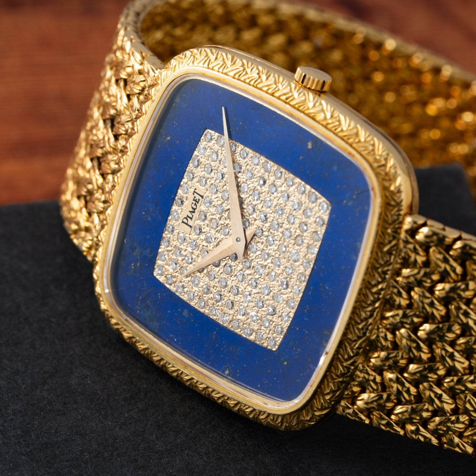 The Piaget Pave Lapis Lazuli Dress Watch features a blue lapis dial, diamond center, and textured gold band, elegantly displayed on a dark surface.