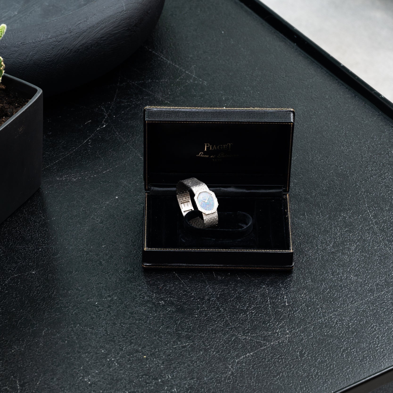 The Opal White Gold Dress Watch by Piaget rests in a black Piaget box on a dark textured table.