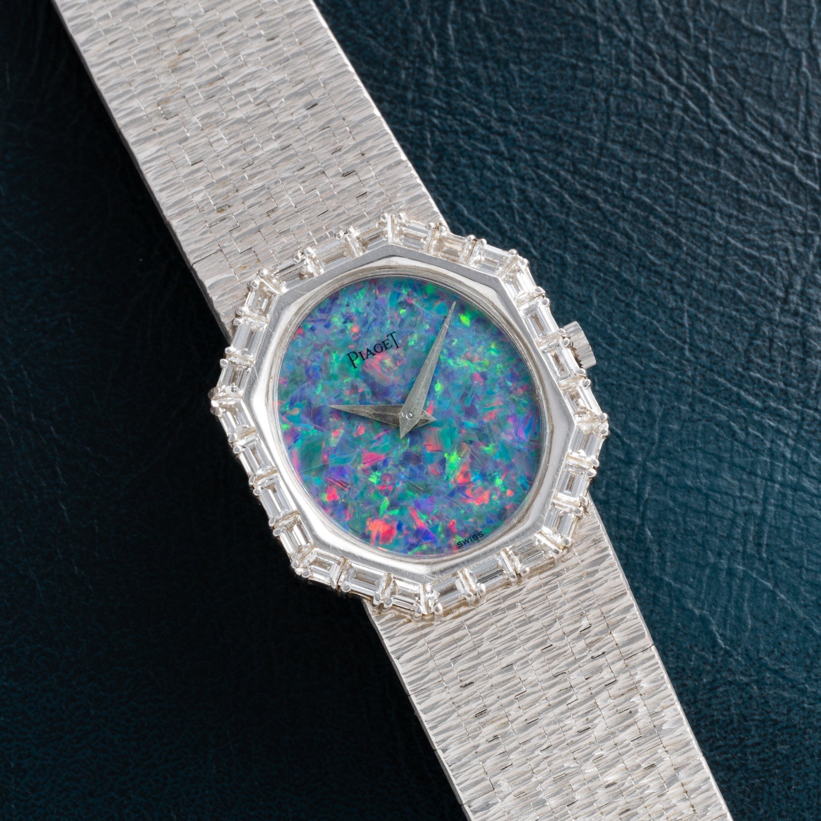 The Piaget Opal White Gold Dress Watch features a colorful opal dial and gem-set bezel, set on a textured band, resting on dark leather.