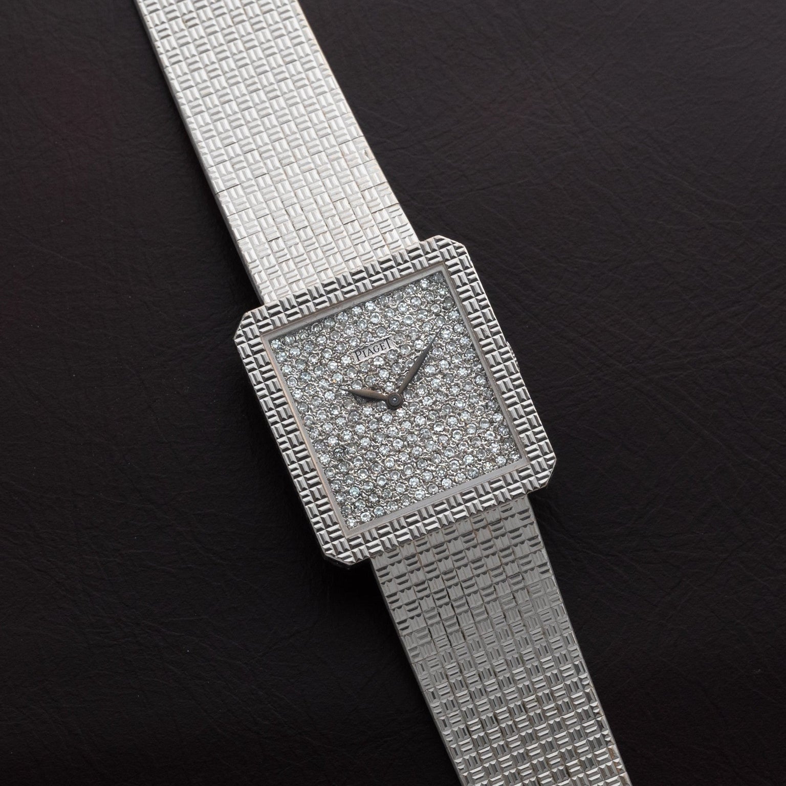 The Piaget Brick Diamond Dress Watch features a square silver face, diamond-studded dial, and textured band, shown on a dark surface.