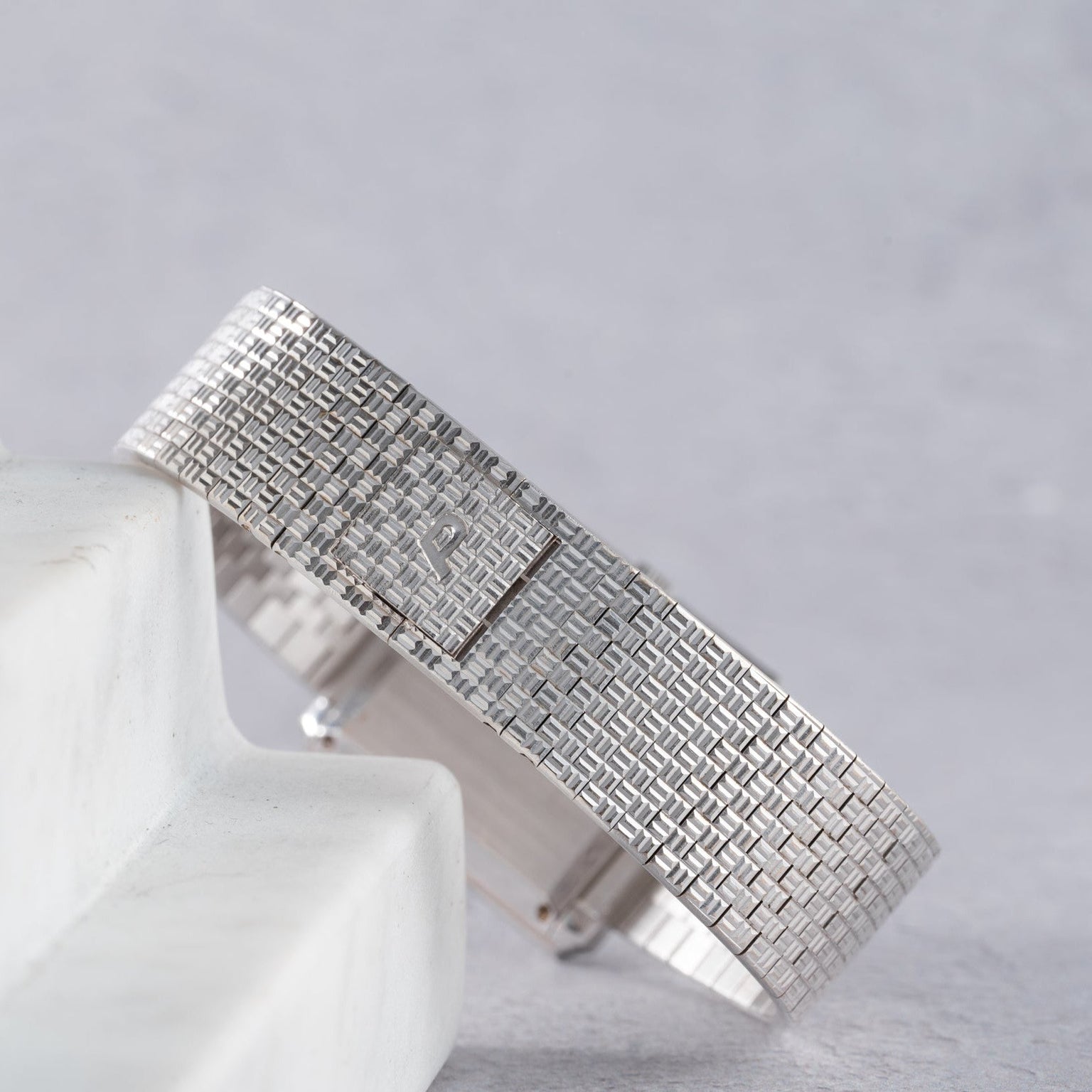 The Piaget Brick Diamond Dress Watch is displayed on a white marble surface with a gray background.