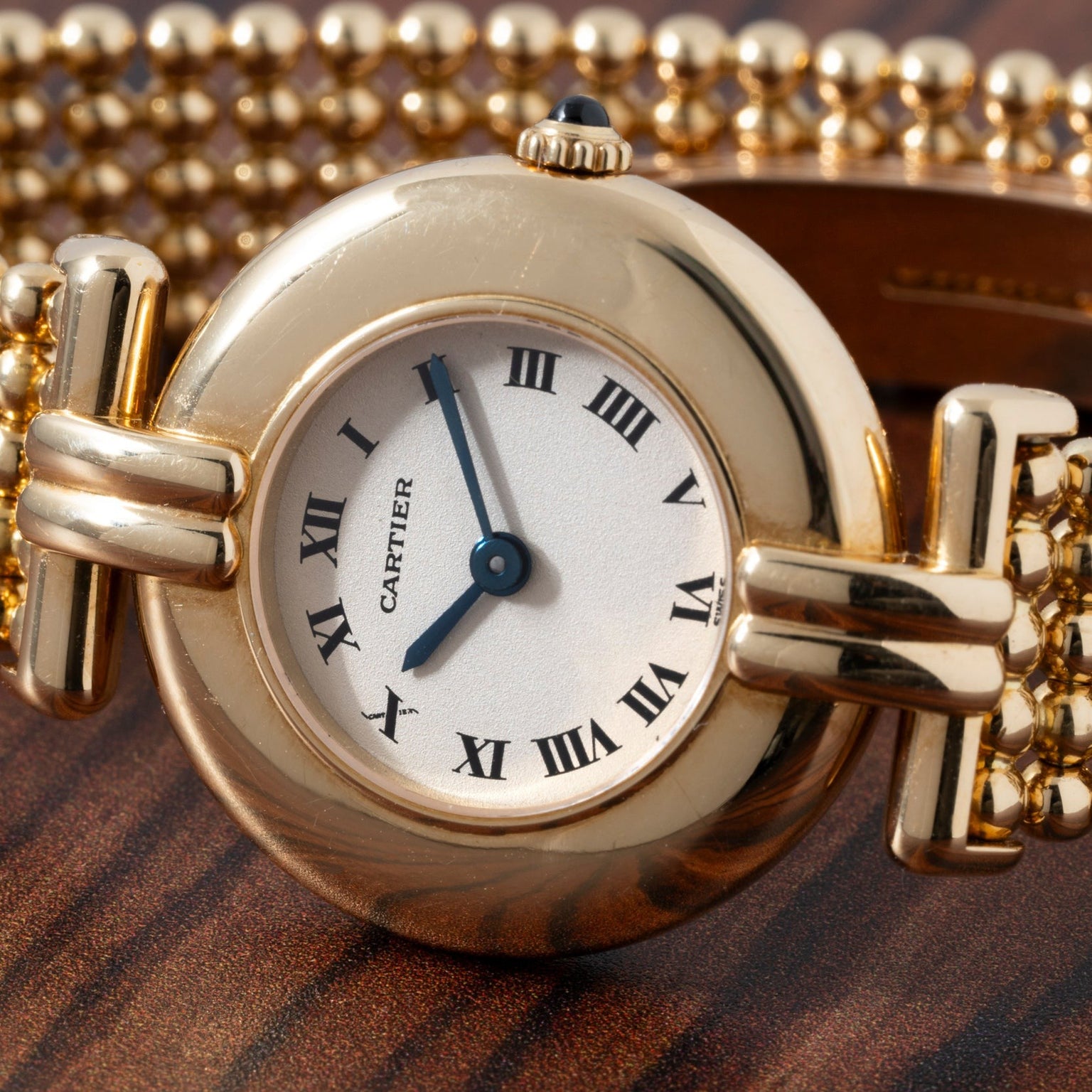 Cartier Ladies Dress Watch with Roman numerals and beaded bracelet displayed on a wooden surface.