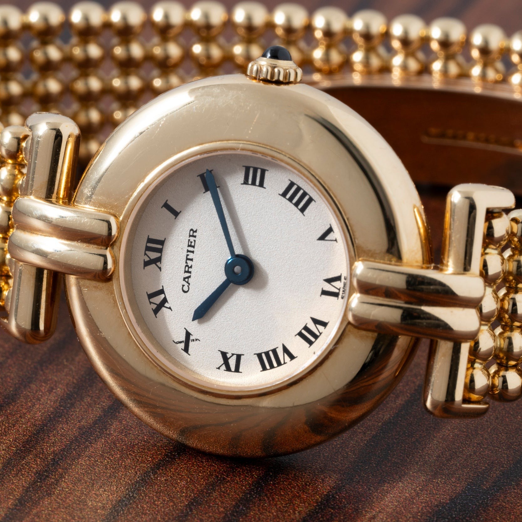 Cartier Ladies Dress Watch with Roman numerals and beaded bracelet displayed on a wooden surface.