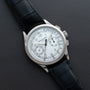 A Patek Philippe Chronograph wristwatch with a white dial and black leather strap displayed on a dark surface.