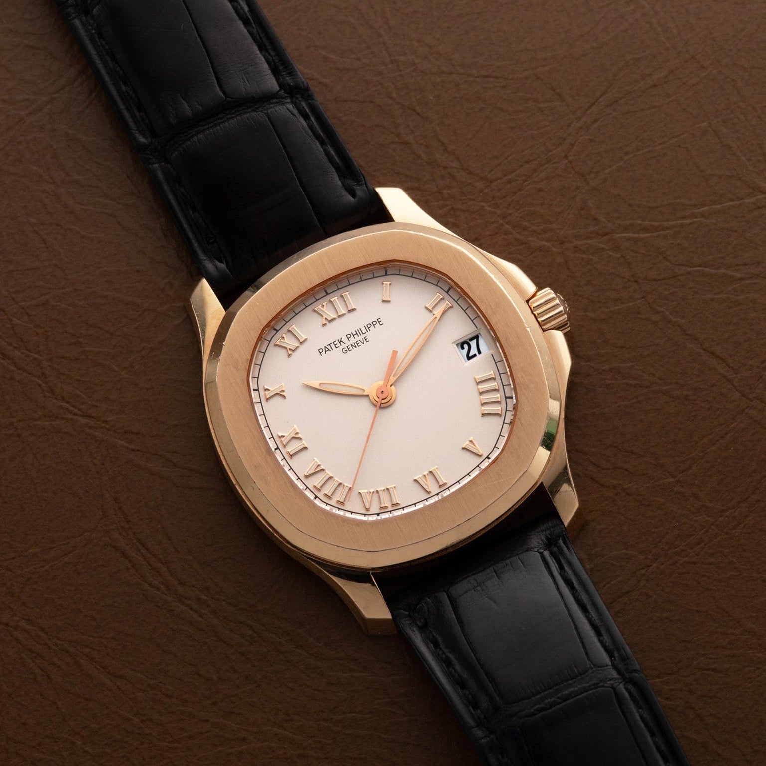 A Patek Philippe Aquanaut watch with Roman numerals and a black leather strap resting on a brown leather surface.