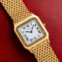 The Cartier Santos Dumont is a gold watch featuring a square face with Roman numerals on a red leather strap.