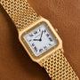 The Cartier Santos Dumont is a gold wristwatch featuring a square face with Roman numerals and a brown leather strap.