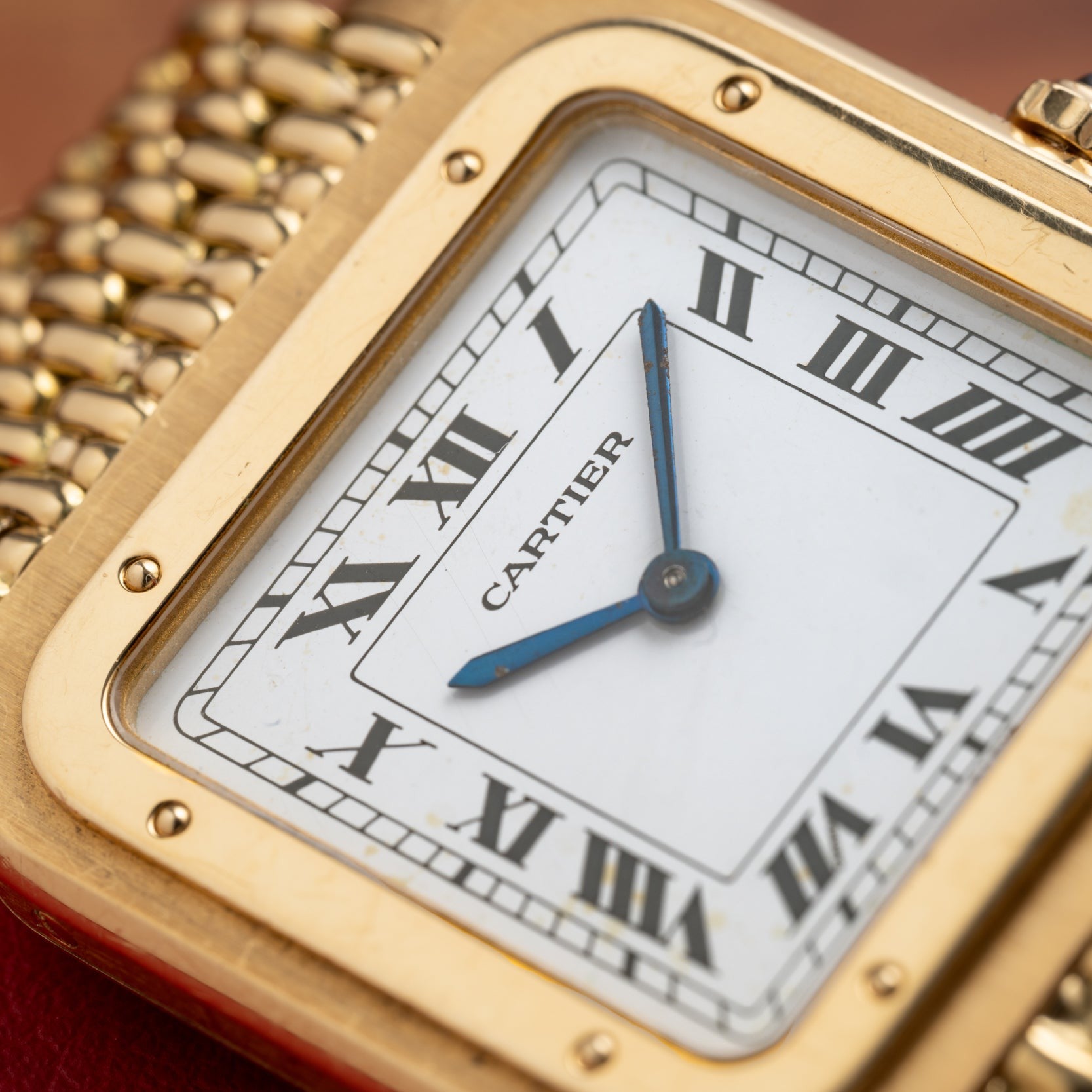 Close-up of a Cartier Santos Dumont gold watch featuring Roman numerals and blue hands on a white dial.