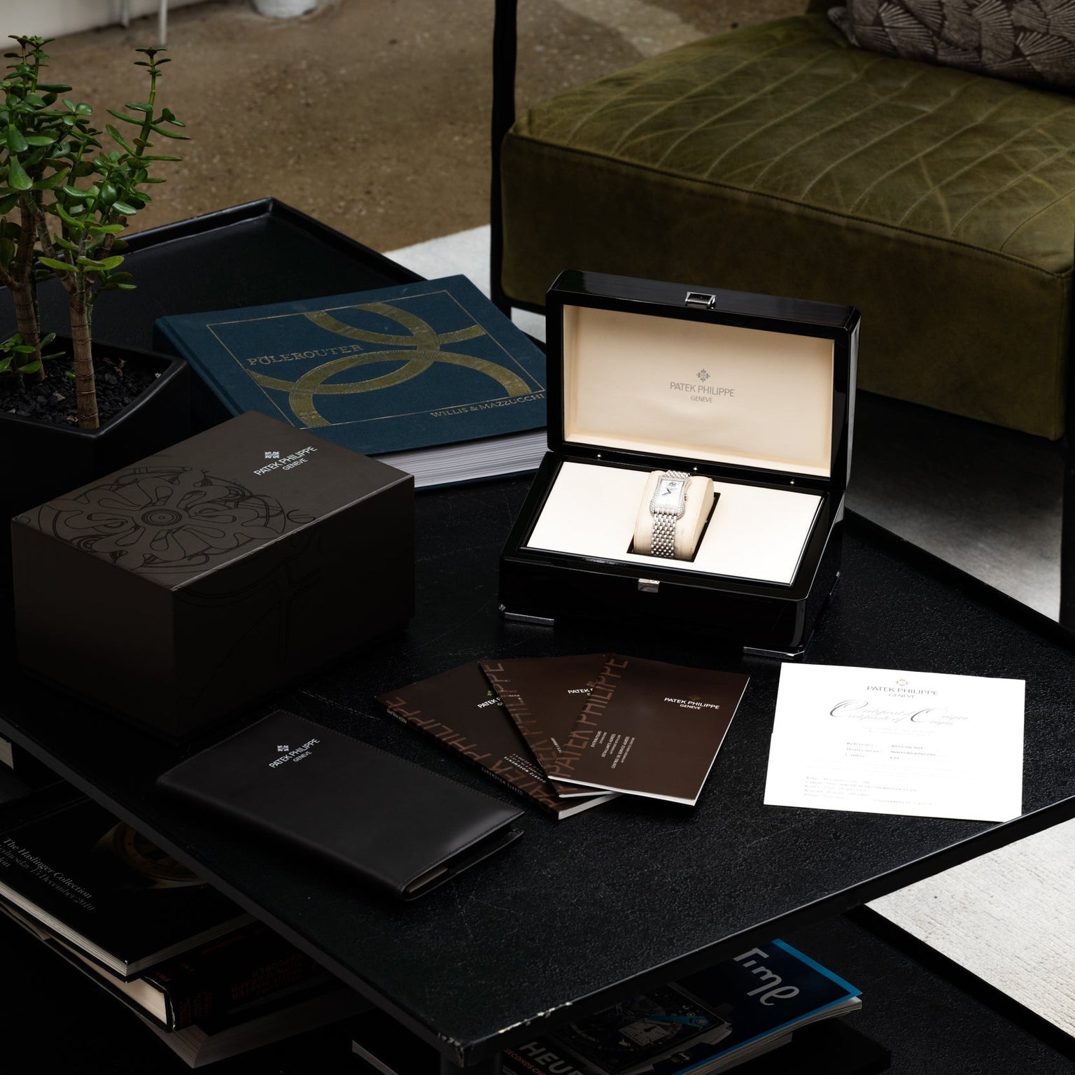 A Patek Philippe Gondolo Ladies watch displayed in an open box, surrounded by booklets and papers on a black table.