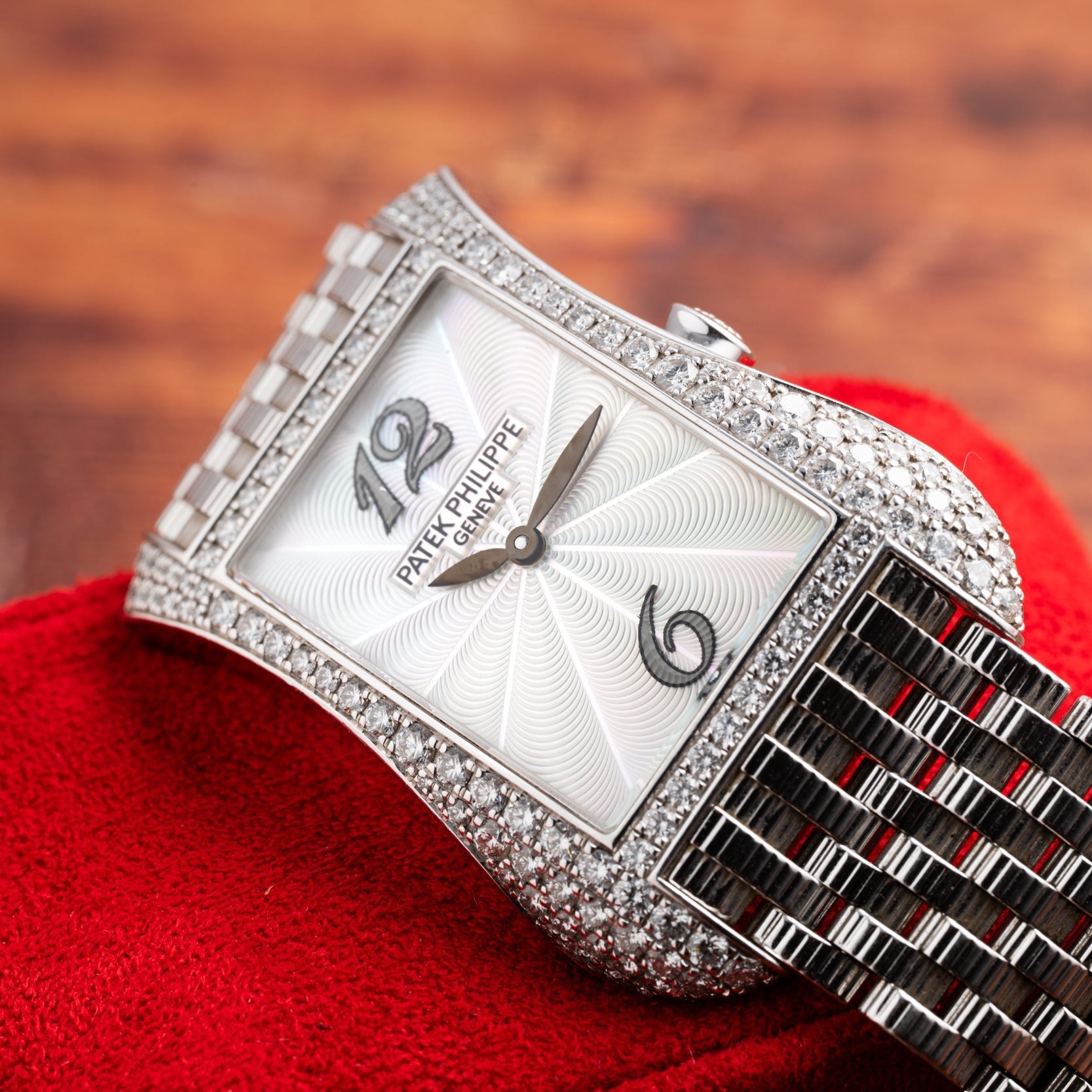Patek Philippe Gondolo Ladies watch with a rectangular diamond-encrusted case and silver bracelet, displayed on red fabric.