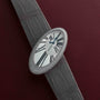 A Cartier Libre Hypnose watch with an oval case, grey strap, and diamond bezel displayed on a burgundy leather surface.