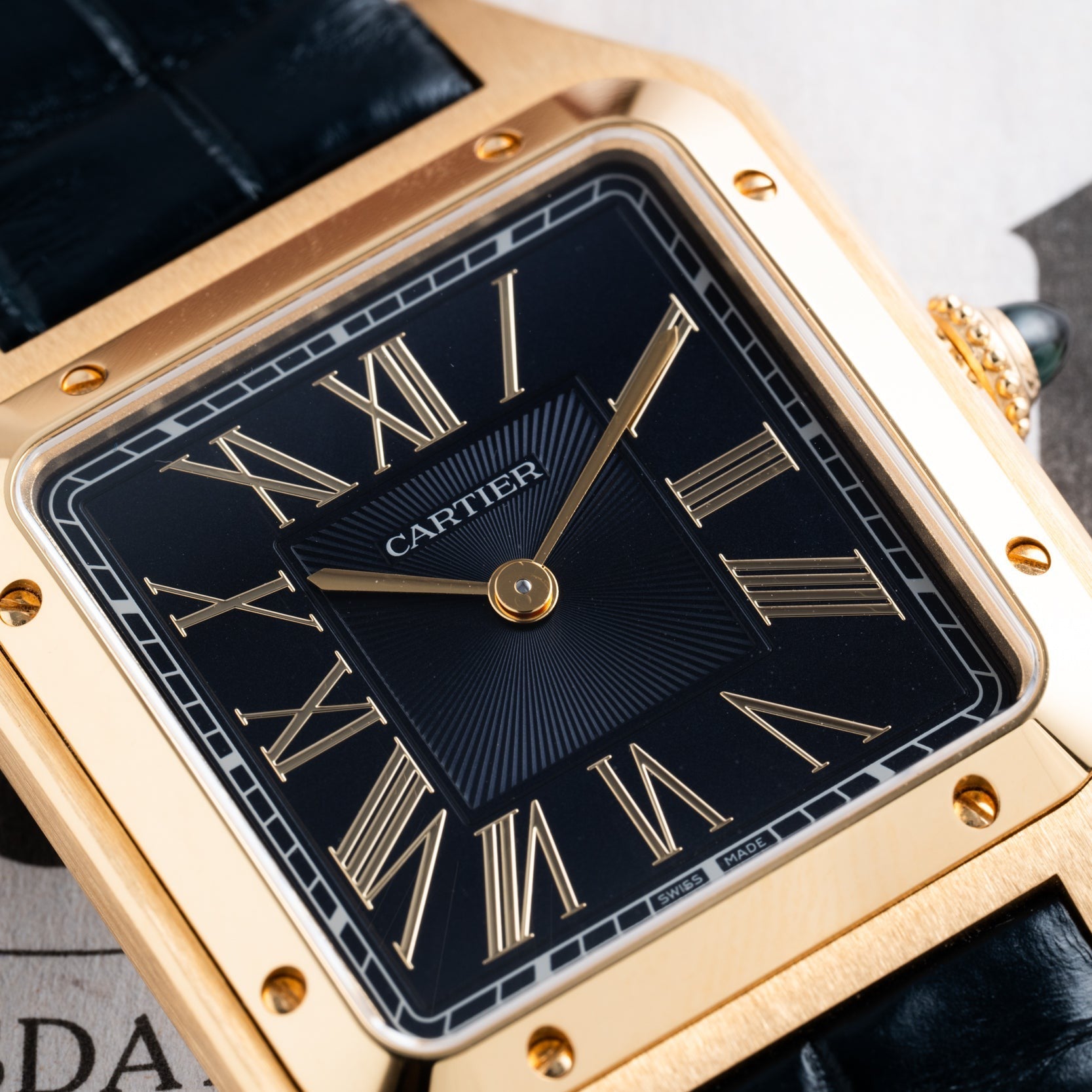 Close-up of the Cartier Santos Dumont gold wristwatch featuring a black face and Roman numeral hour markers.