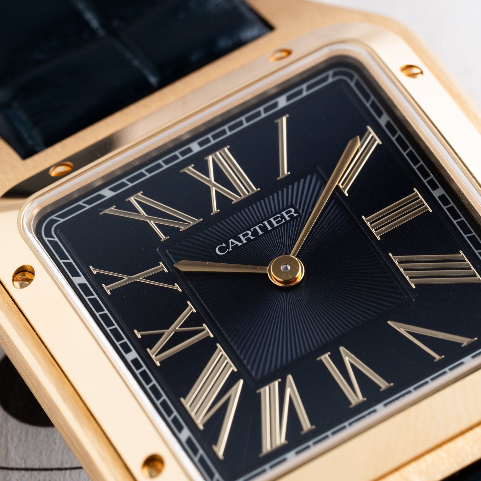 Close-up of a Cartier Santos Dumont watch face featuring gold Roman numerals on a black background.