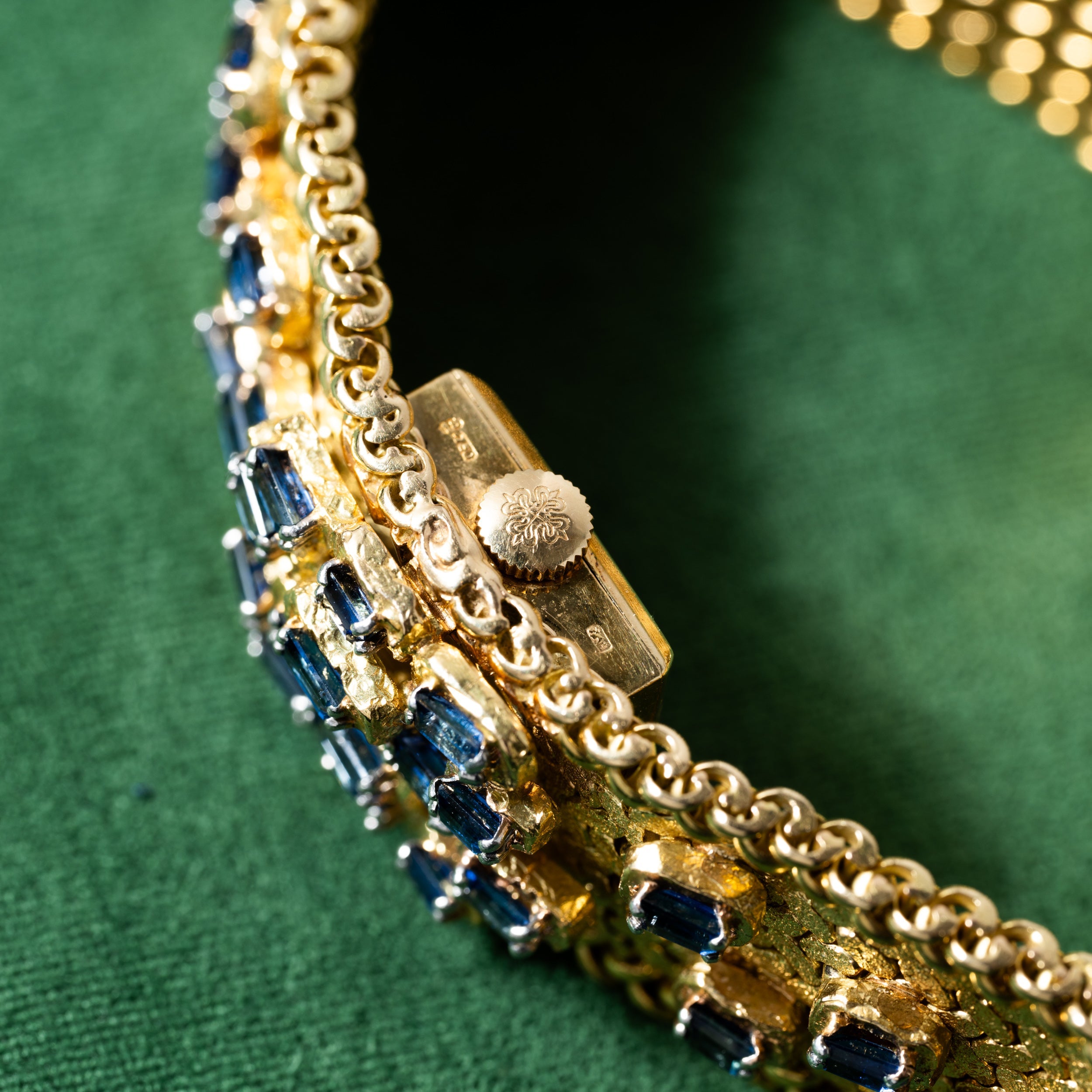 Close-up of a Patek Philippe Yellow Gold Integrated Dress Watch with a decorative clasp, displayed against a green fabric background.