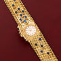 Patek Philippe Yellow Gold Integrated Dress Watch, featuring a textured band and blue gemstones, displayed on a dark red leather surface.