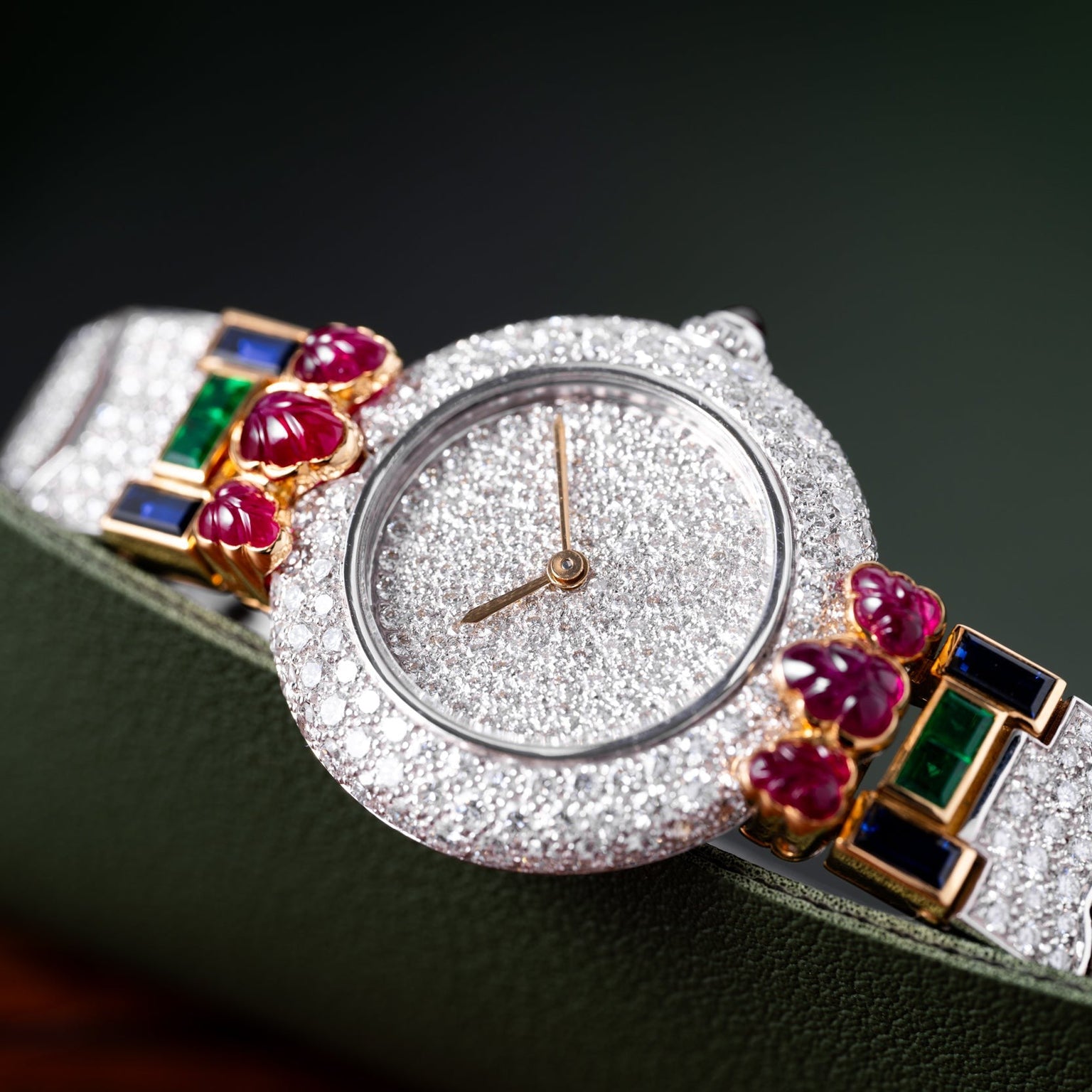 The Cartier Colisee Tutti Frutti Diamond watch, adorned with diamonds, rubies, and emeralds, is displayed on a green surface.