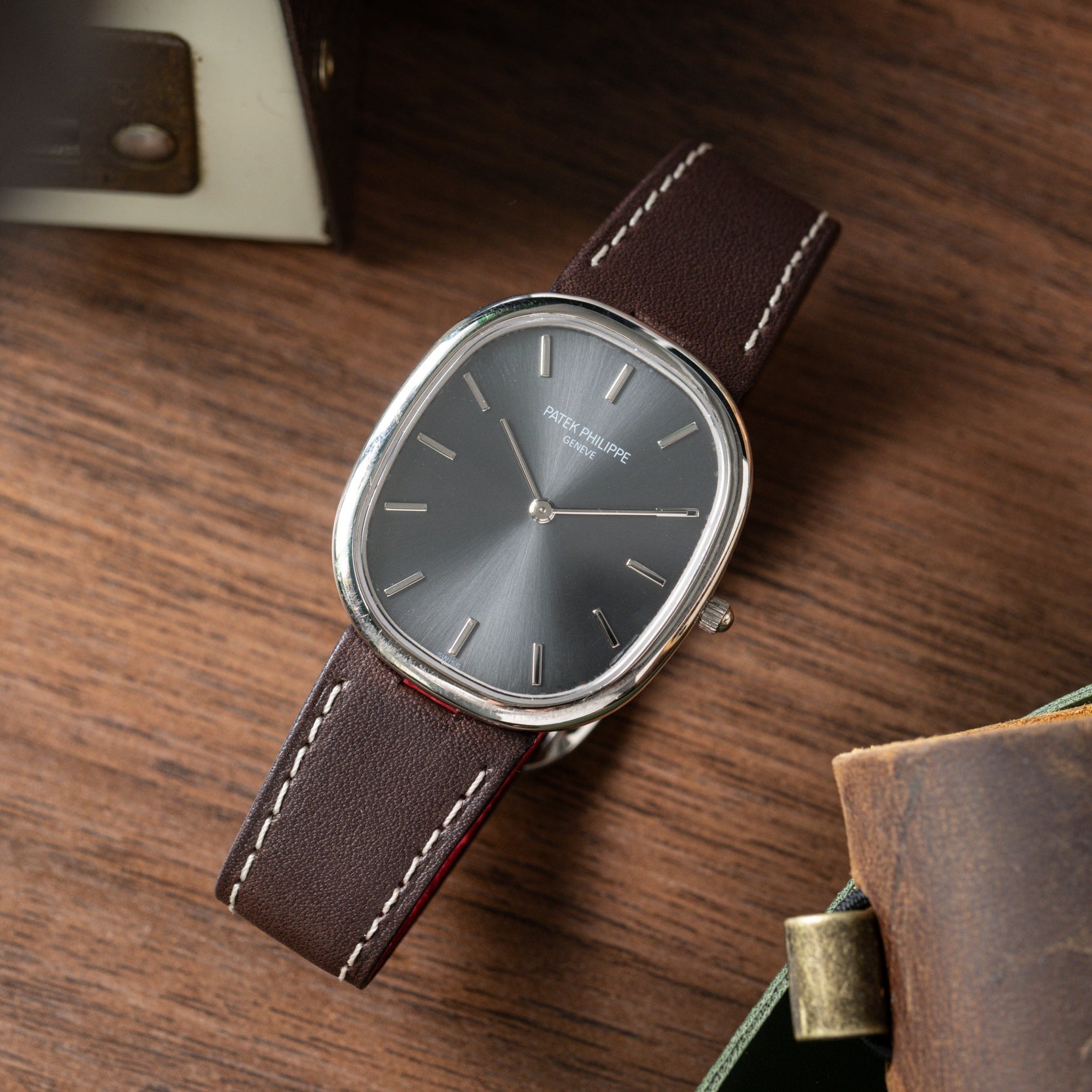 The Patek Philippe Ellipse watch with a brown leather strap rests on a wooden surface.
