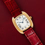 A Cartier Gondole Ladies gold watch with a red leather strap rests on a matching red leather surface.