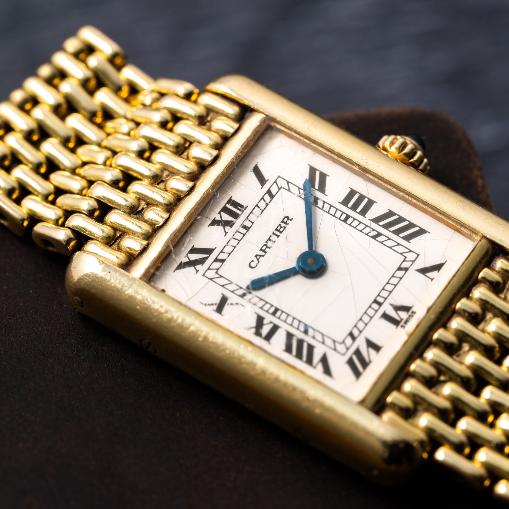 Close-up of the Cartier Tank Louis gold wristwatch, featuring a rectangular face with Roman numerals, set against a dark background.