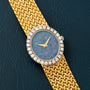 The Piaget Opal Yellow Gold Dress Watch features a jeweled bezel and opal face, elegantly displayed on a dark textured surface.