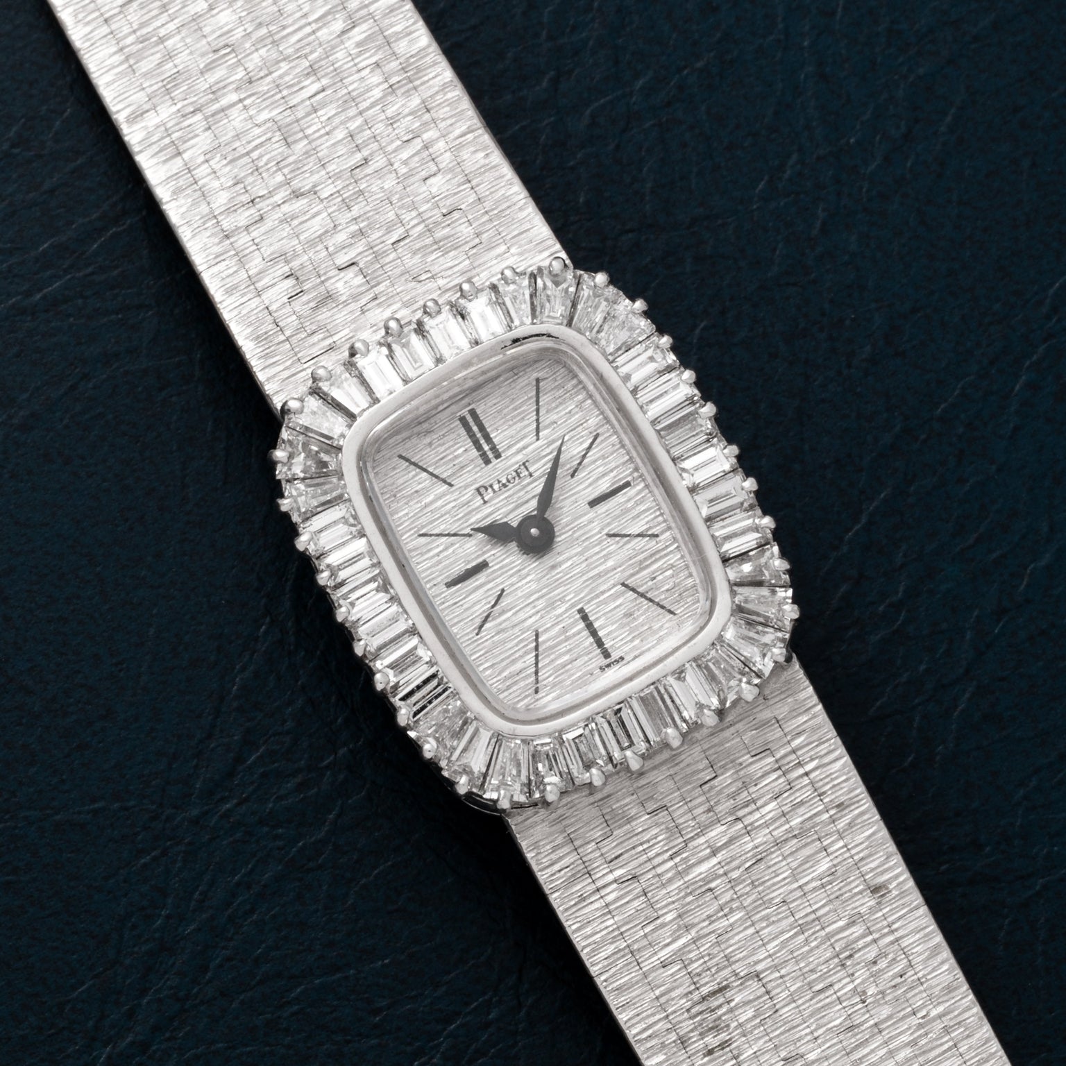 A Piaget White Gold Bark Diamond Dress Watch with a textured band and diamond-set rectangular face rests on a dark surface.