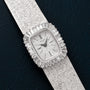 A Piaget White Gold Bark Diamond Dress Watch with a textured band and diamond-set rectangular face rests on a dark surface.