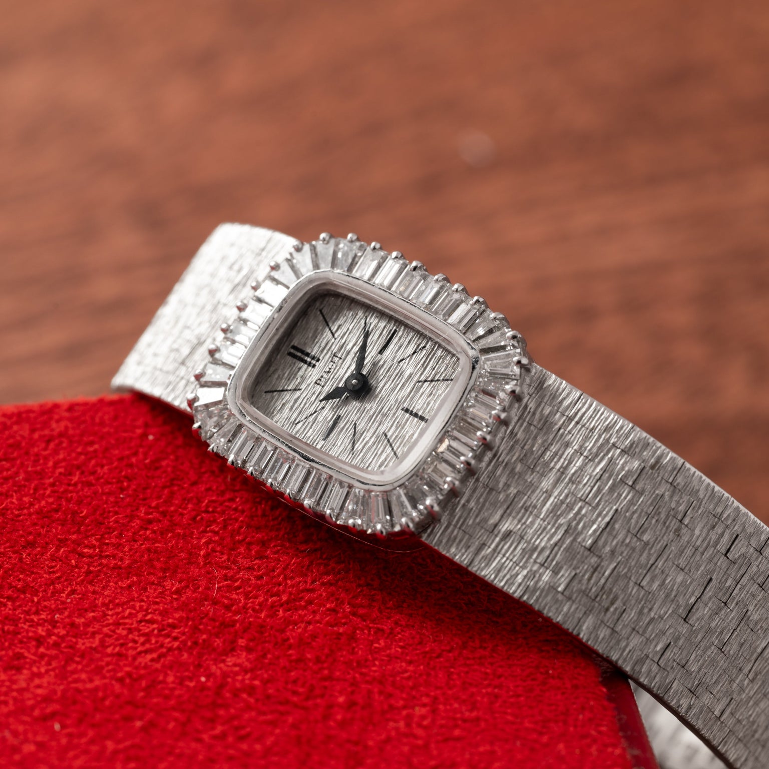 A Piaget White Gold Bark Diamond Dress Watch with a textured band and bezel rests on a red surface.