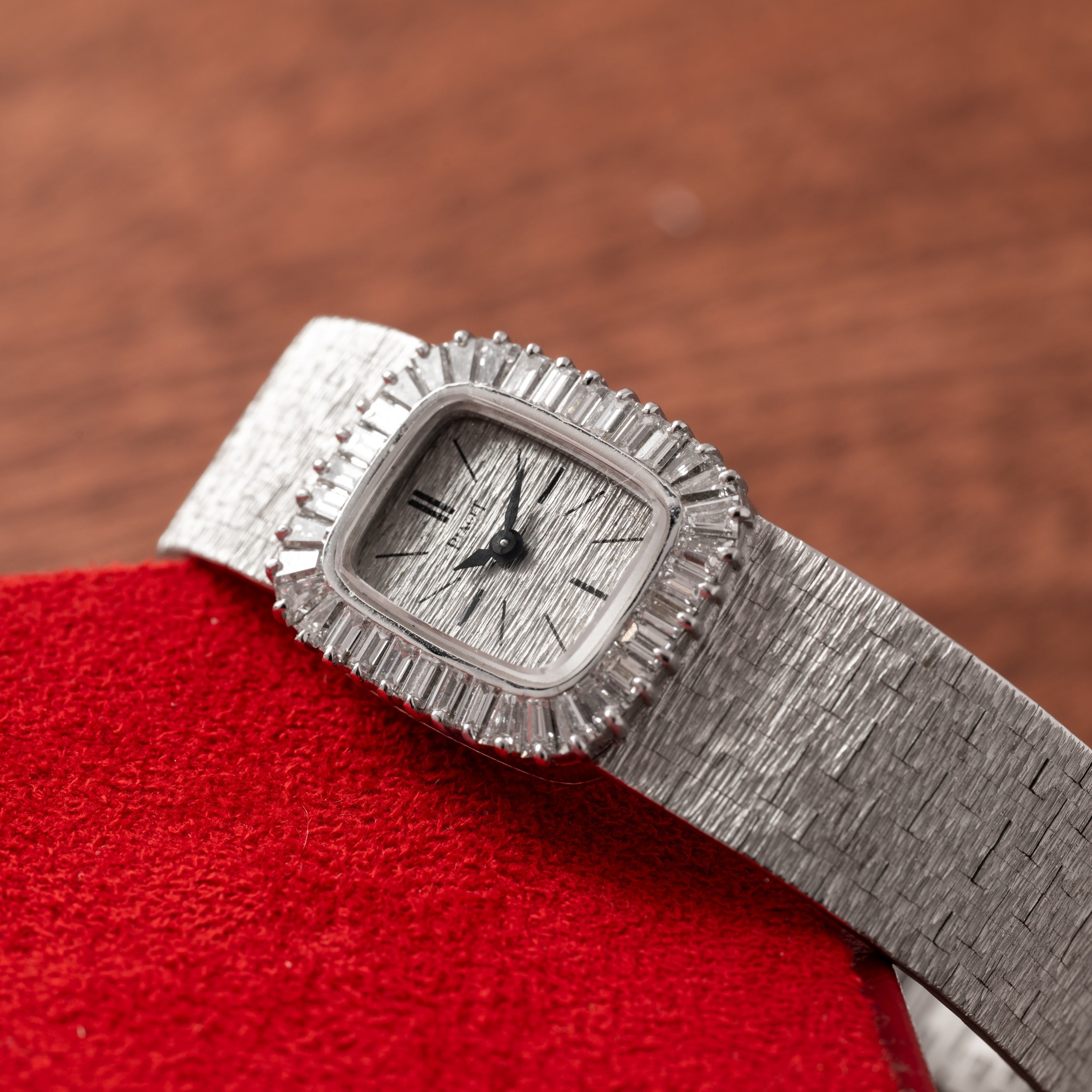 A Piaget White Gold Bark Diamond Dress Watch with a textured band and bezel rests on a red surface.
