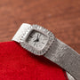 A Piaget White Gold Bark Diamond Dress Watch with a textured band and bezel rests on a red surface.