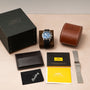 A Breitling SuperOcean B01 Chronograph 44 watch, complete with box, case, extra strap, and documents, is arranged neatly on a light surface.