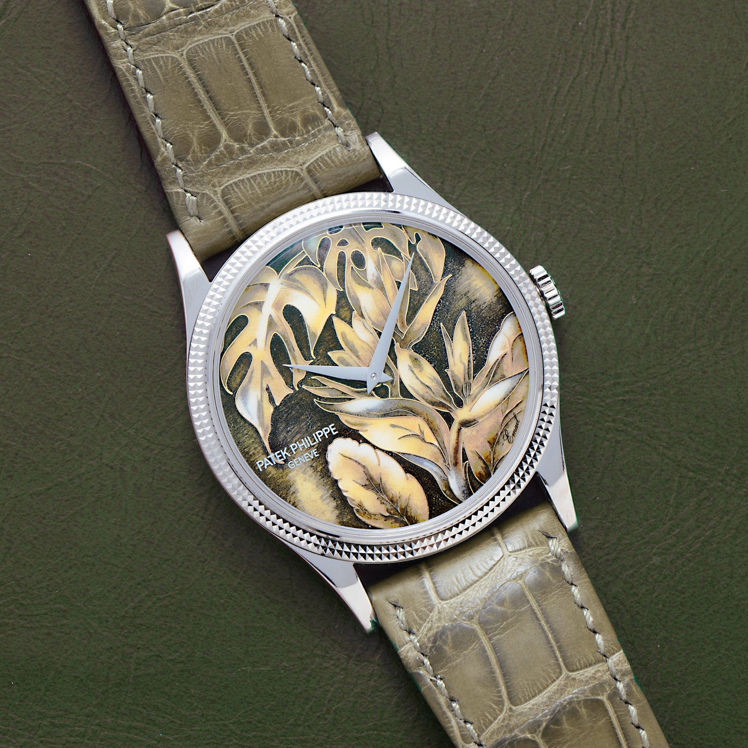 The Patek Philippe Calatrava Cloisonné Tropical Leaves II is a luxury watch with a green leather strap and an intricate leaf-patterned dial in earthy tones.