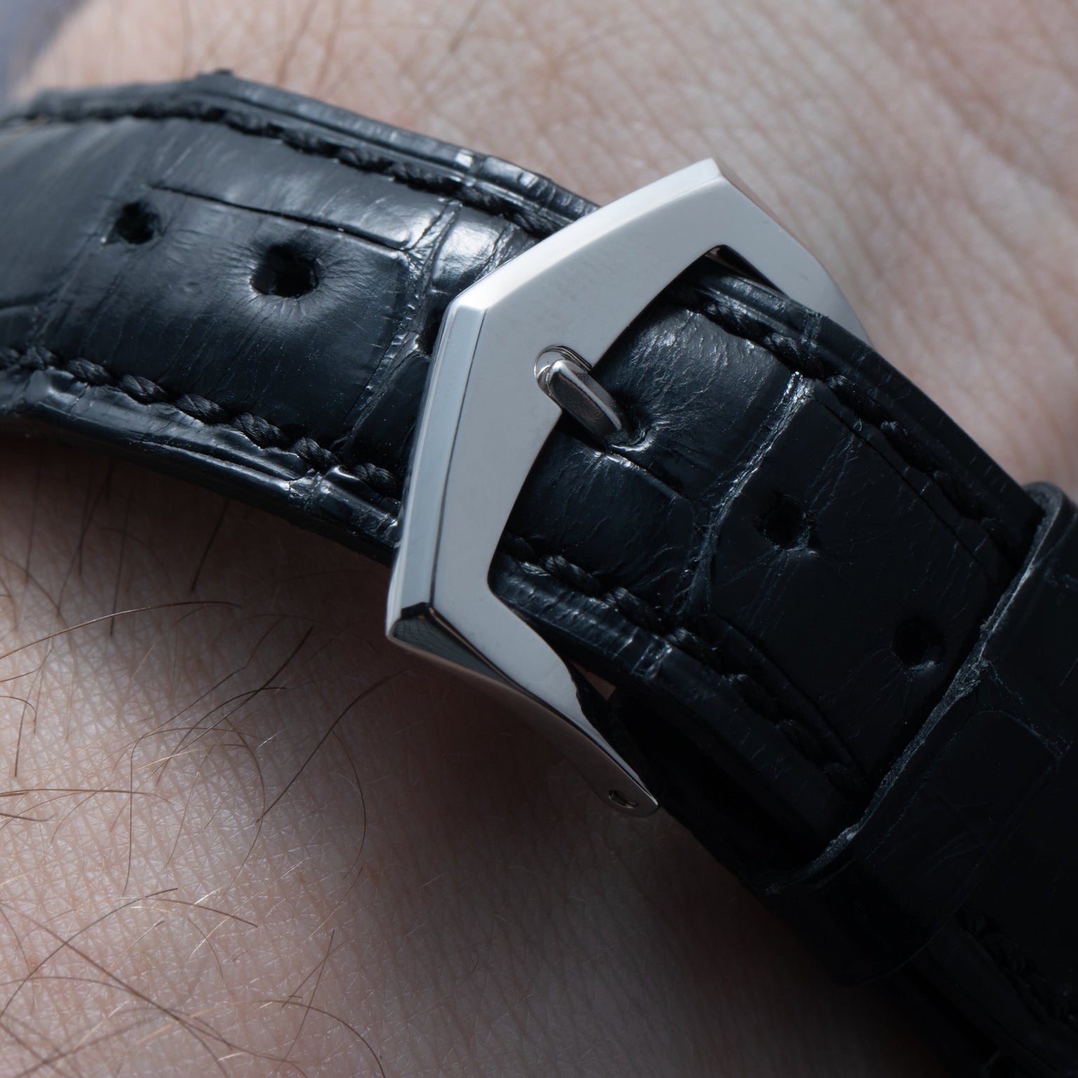 A close-up of the Patek Philippe Calatrava Cloisonné Iris & Night Fireflies black leather watch strap with a silver buckle on a persons wrist.