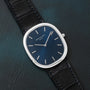 A Patek Philippe Ellipse Jumbo watch with a blue face and black leather strap rests on a dark textured surface.