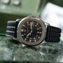 The Patek Philippe Aquanaut, a silver wristwatch with a black rubber strap, is displayed on a green marble surface.