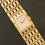 Piaget Dancer gold wristwatch with a diamond-studded square face, displayed on a dark textured surface.