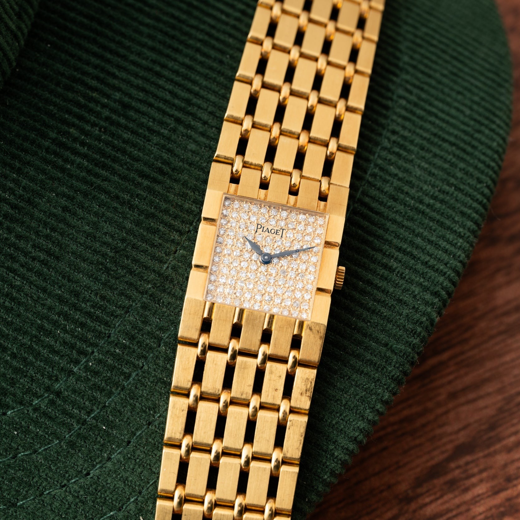 A Piaget Dancer gold watch with a diamond-studded face rests on a green textured surface.