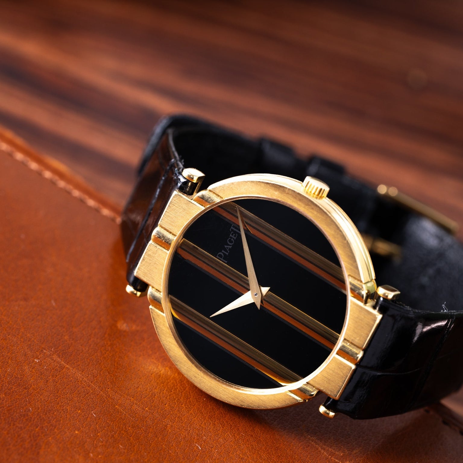 The Piaget Polo Onyx gold wristwatch with a black strap is displayed on a brown leather surface.