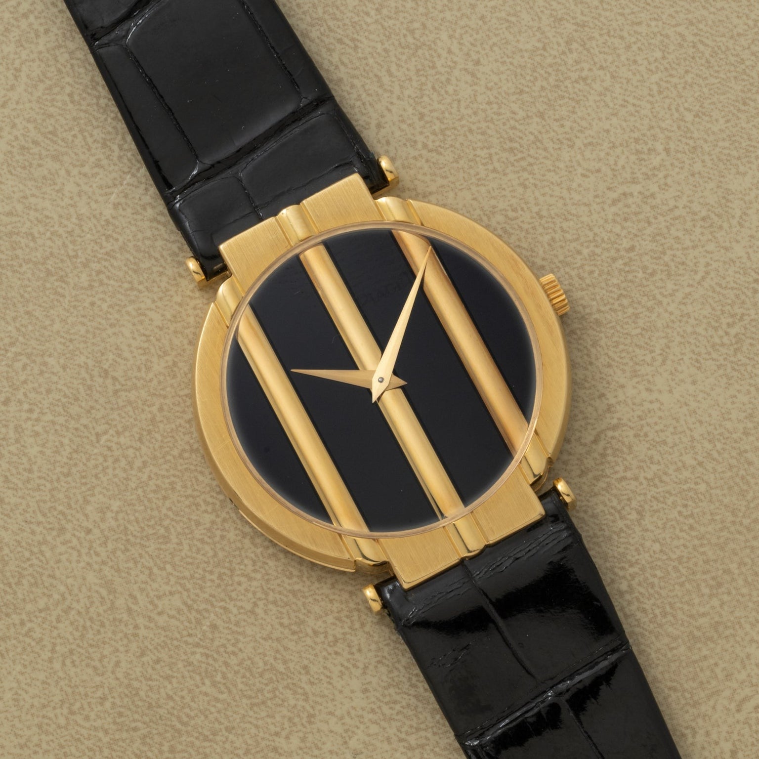 Piaget Polo Onyx gold wristwatch with a black face, three vertical gold bars, and a black leather strap displayed on a beige surface.