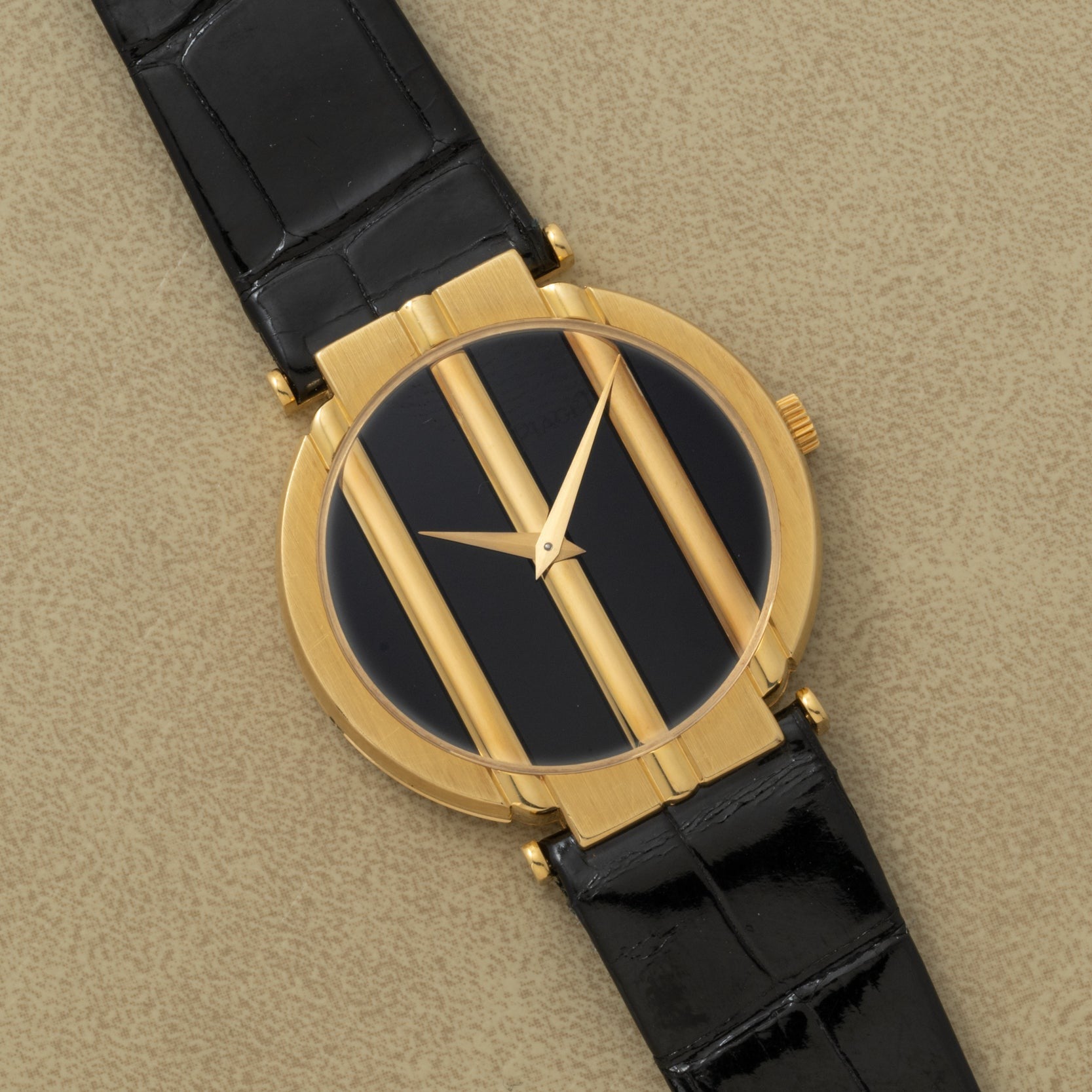 Piaget Polo Onyx gold wristwatch with a black face, three vertical gold bars, and a black leather strap displayed on a beige surface.