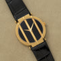 Piaget Polo Onyx gold wristwatch with a black face, three vertical gold bars, and a black leather strap displayed on a beige surface.
